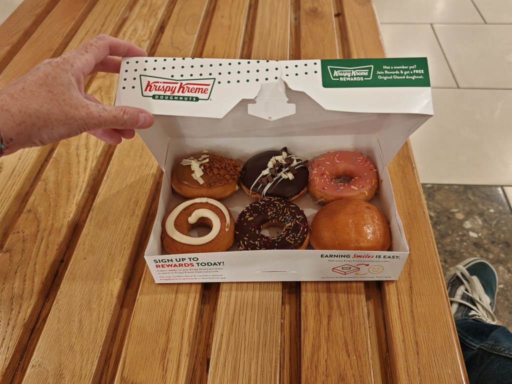 A selection box of 6 Krispy Kreme doughnuts on a bench in a shopping centre