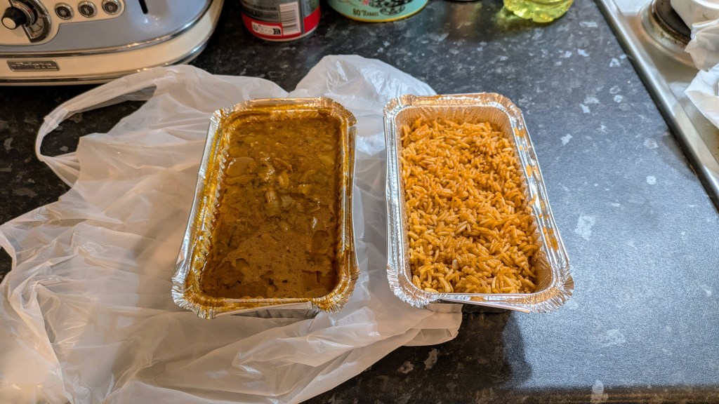 A aluminium container of peanut butter stew with chicken next to one filled with jollof rice