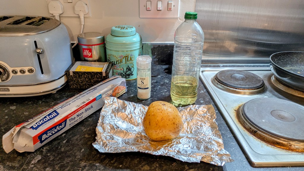 A jacket potato on tinfoil, next to a bottle of oil, salt, and spices
