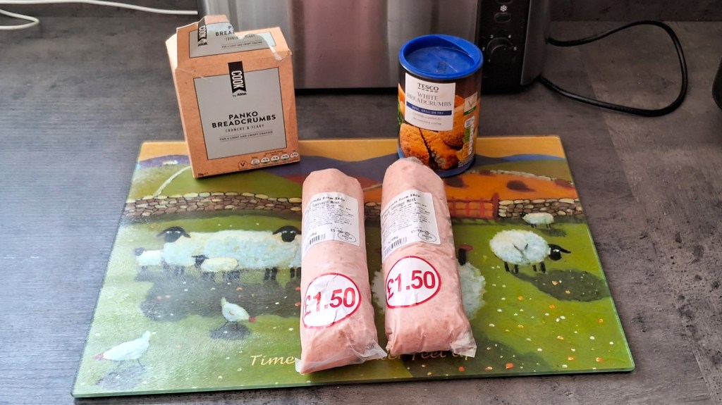Two packs of sausage meat and two types of breadcrumb boxes on a chopping board
