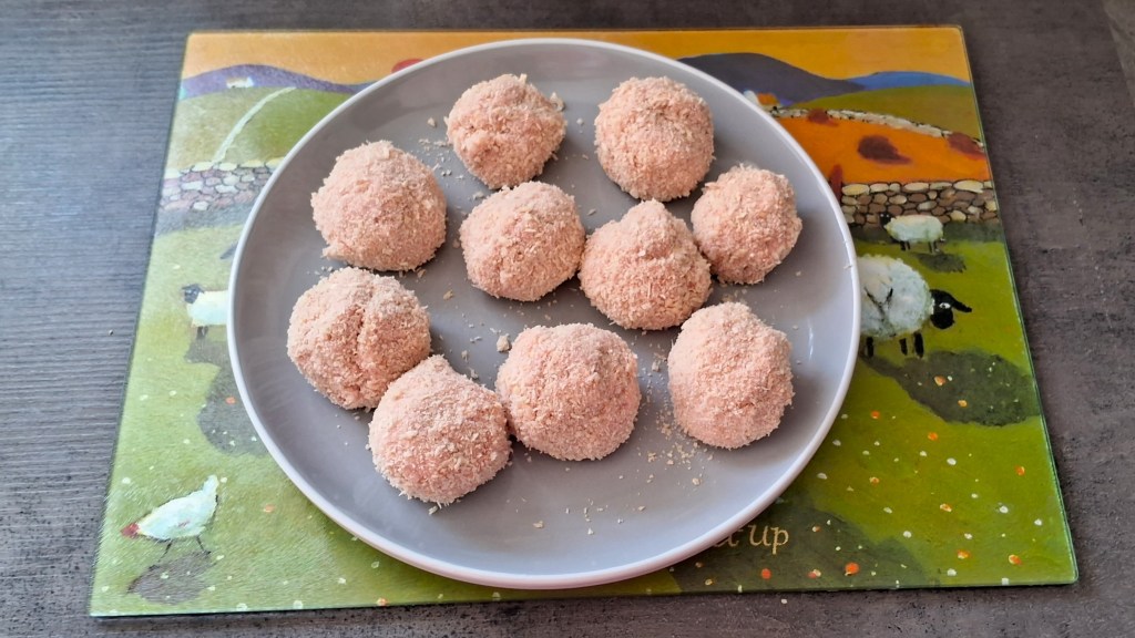 Uncooked sausage meat coated in breadcrumbs on a plate