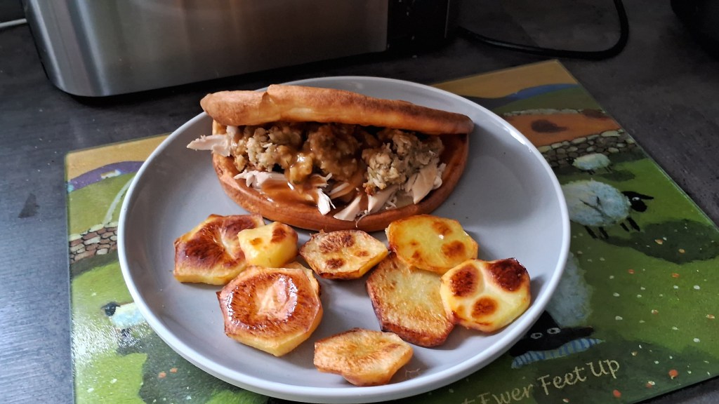 The finished yorkshire pudding wrap on a plate stuffed with chicken and stuffing with crispy sliced potatoes next to it