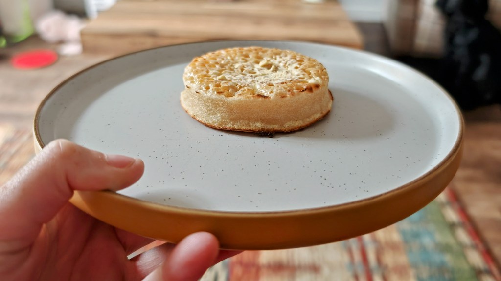 A single buttered crumpet on a yellow rimmed plate