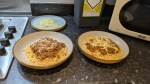 Two bowls of spaghetti bolognese with cheese and parmesan on a worktop