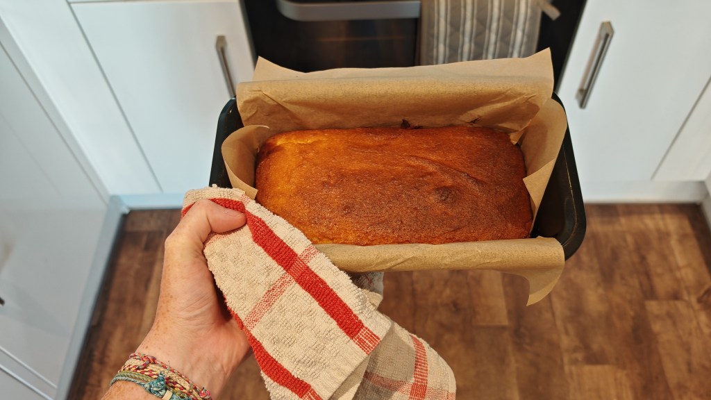 The Groovy Keto Lemon Cake in a loaf tin, being held by a teatowel