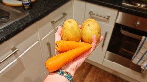 Holding two carrots and two potatoes in a kitchen